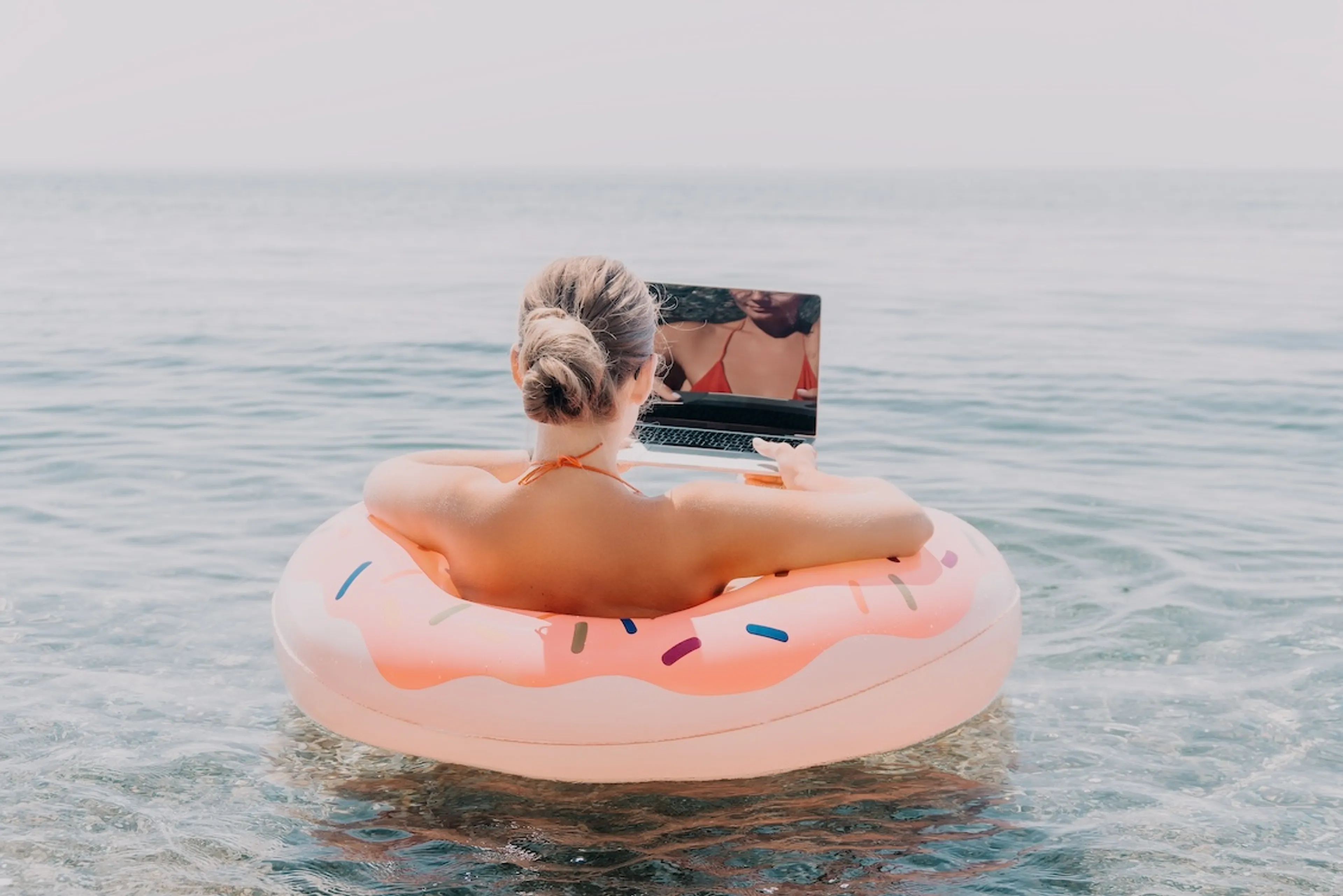 Vrouw die in een zwembad aan het werk is op haar laptop, terwijl ze in de zee dobbert.