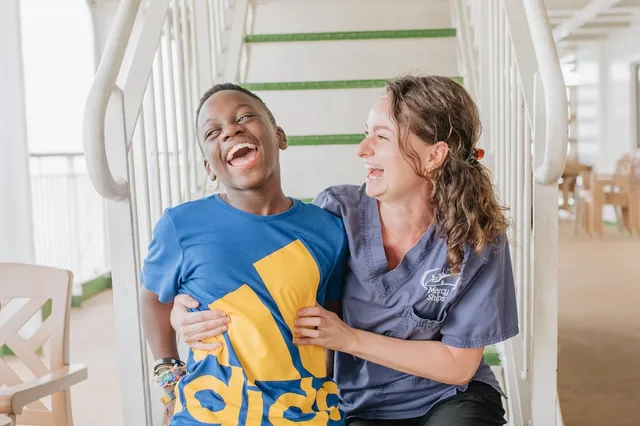 Dieke van Tuijl in haar werkkleding op Mercy Ships samen met een patiënt.
