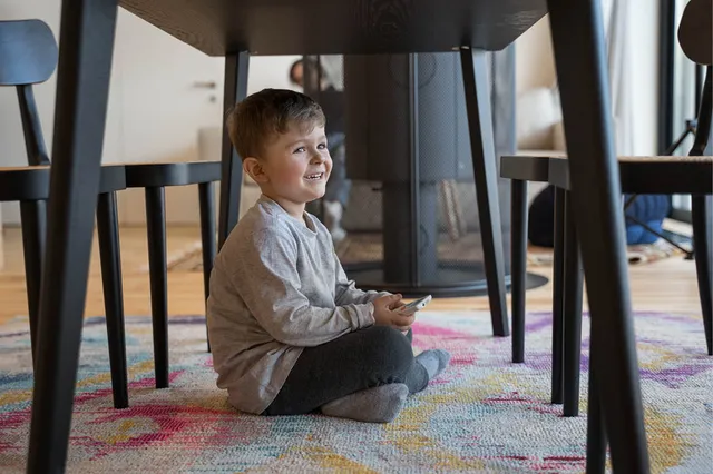 Jongen van 5 jaar onder de tafel, lacht ondeugend.