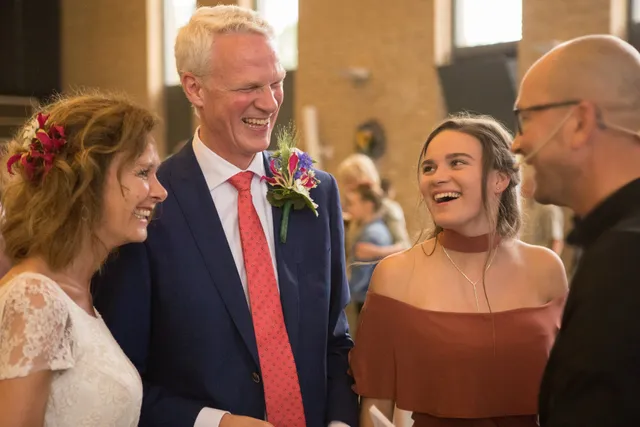 Anne-Renske op de bruiloft van Nancy en haar vader. Ze staan in een kerk en lachen naar elkaar.