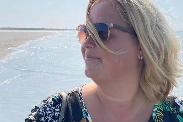 Jolanda staat met een zonnebril op op het strand met de zon in haar gezicht.