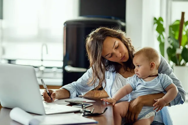 Vrouw met baby op schoot, ze probeert te werken en zit achter de laptop.