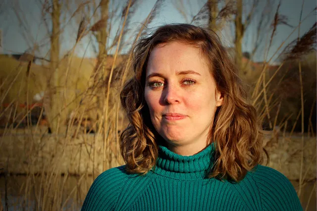 Nanette staat in de zon voor een natuurlijke achtergrond met riet en kijkt serieus in de camera.