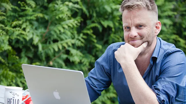 Wilfred zit met zijn laptop buiten en kijkt glimlachend in de camera.