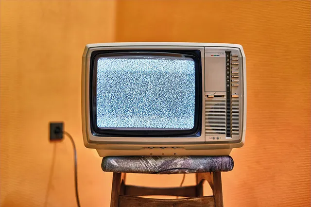 Tv met sneeuw op een krukje en een jaren 60 oranje behang.