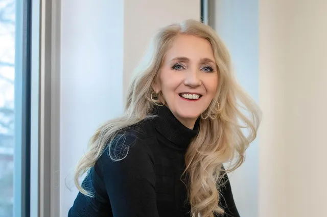 Seksuoloog Astrid Kremers heeft lang blond haar in een slag en een zwarte coltrui aan. Ze zit in een raam en lacht in de camera.