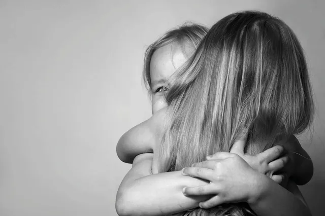 Zwart-wit foto van twee kleinere meisjes die elkaar omhelzen. Je ziet vooral de achterkant van het hoofdje.