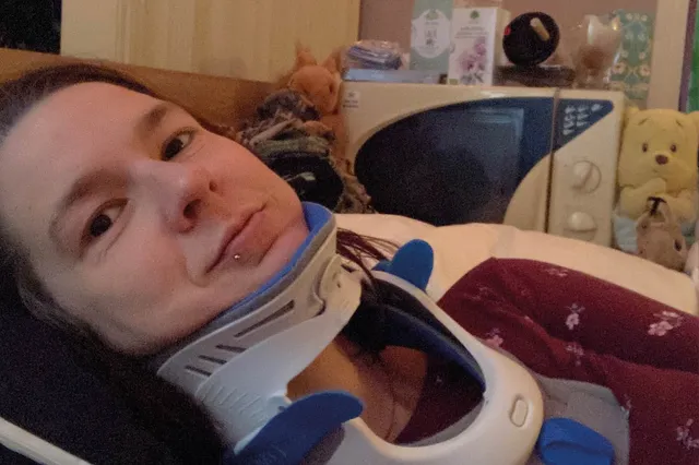 Annemarie ligt op bed. Ze heeft een nekbrace om en naast haar staat een magnetron.