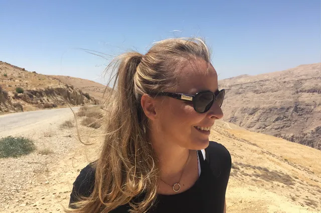 Op de foto staat Daphne met een zonnebril op voor een zandvlakte. Ze kijkt lachend weg van de foto.