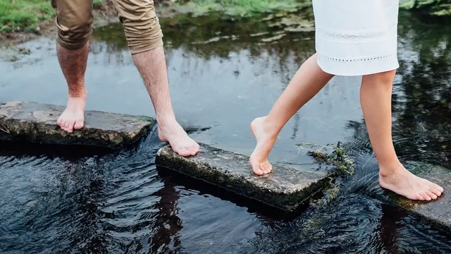 Schoenen uit, sokken uit, blote voeten op stapsteentjes in het water tijdens een blotevoetenpad.