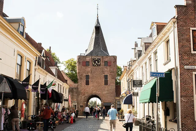 Een van de leukste steden van Nederland om te bezoeken in de zomer is Elburg. Een oude vestingstad met gezellige straatjes en een robuuste kasteelmuur. Er lopen wat mensen door de straat, de zon schijnt en de lucht is blauw.