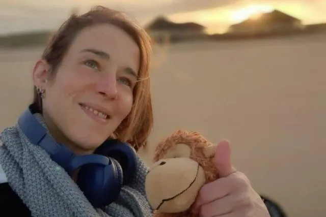 Ellen op het strand met een knuffel in haar hand en koptelefoon om haar nek waar ze aan Eva vertelt over haar dochter die euthanasie kreeg.