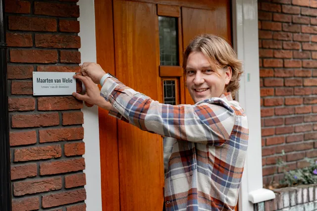 Maarten staat met zijn handen bij een deurbordje naast zijn deur.