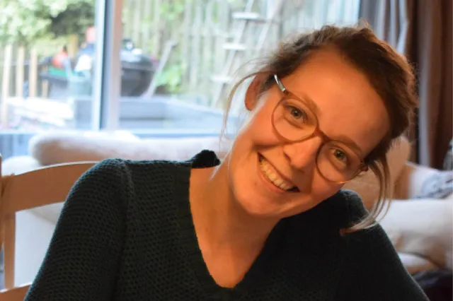 Op de foto staat Hilde lachend. Ze heeft een bril op en haar haar zit in een staart.