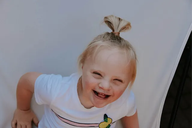 Livia, een meisje met het Syndroom van Down, kijkt omhoog in de camera en lacht.