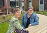 Wilma en Carolien wonen in een noabershof. De twee hebben kort grijs haar, zitten aan een picknicktafel en dragen een bril. Ze lachen naar de camera.