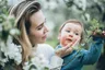 Op de foto staat een moeder met haar zoontje in haar arm in een tuin. Ze heeft haar hand op zijn wang terwijl hij een tak vasthoudt.